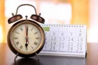 A bronze alarm clock and small desk calendar.
