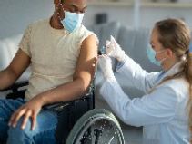 A man in a wheelchair receiving a vaccine injection from a female doctor.