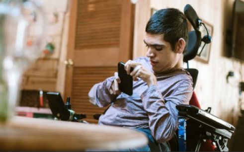 Young man in a wheelchair using a cell phone.
