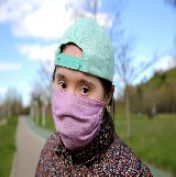 A woman wearing a teal backwards cap and a pink mask.