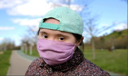 A girl wearing a teal backwards cap and a pink mask.