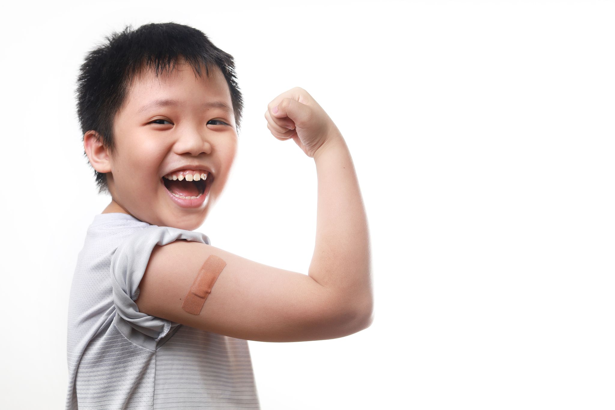 A boy celebrating his vaccination by displaying the bandage. He is smiling.