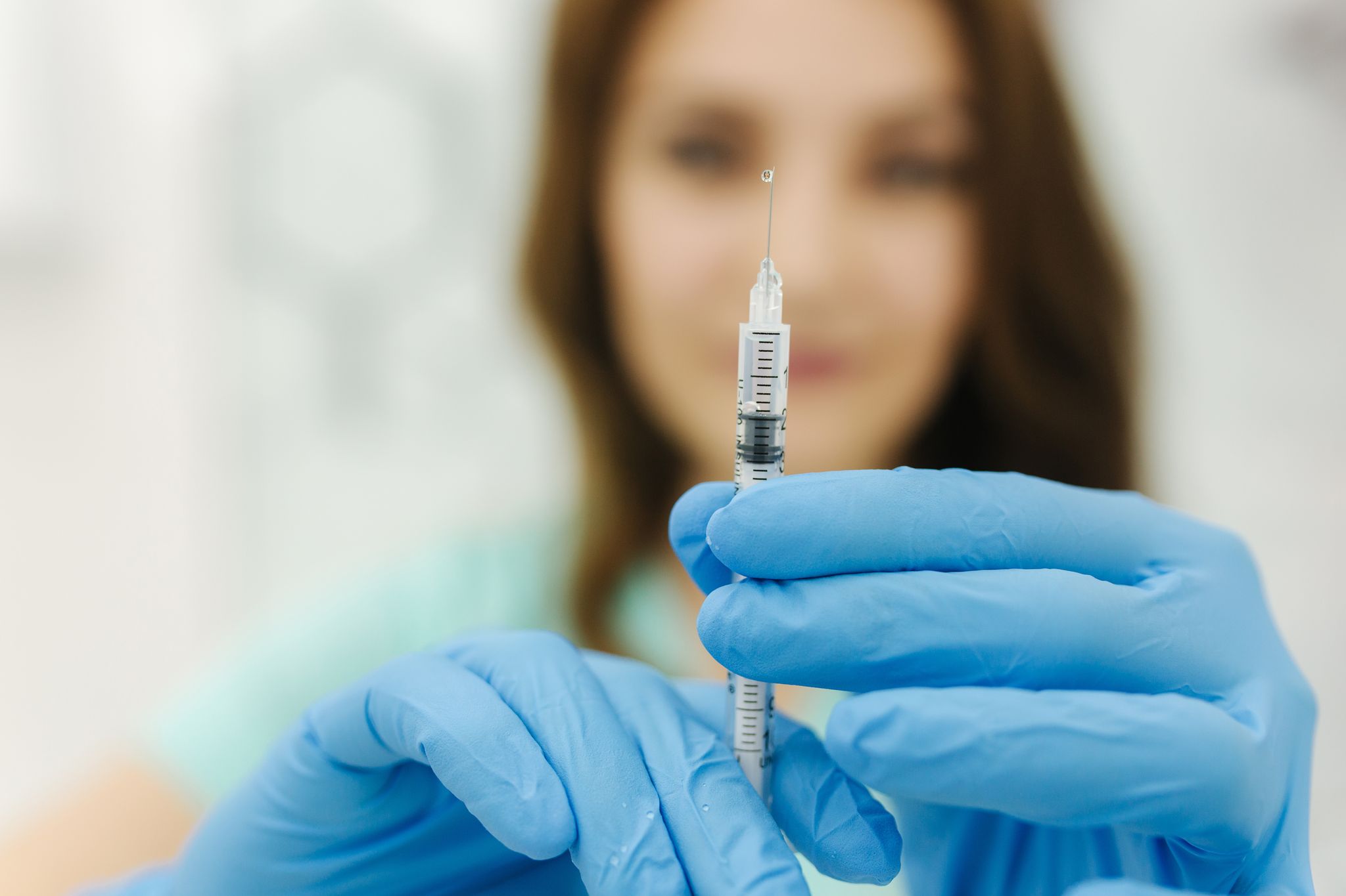A doctor holding a needle toward the camera. The needle is in focus.